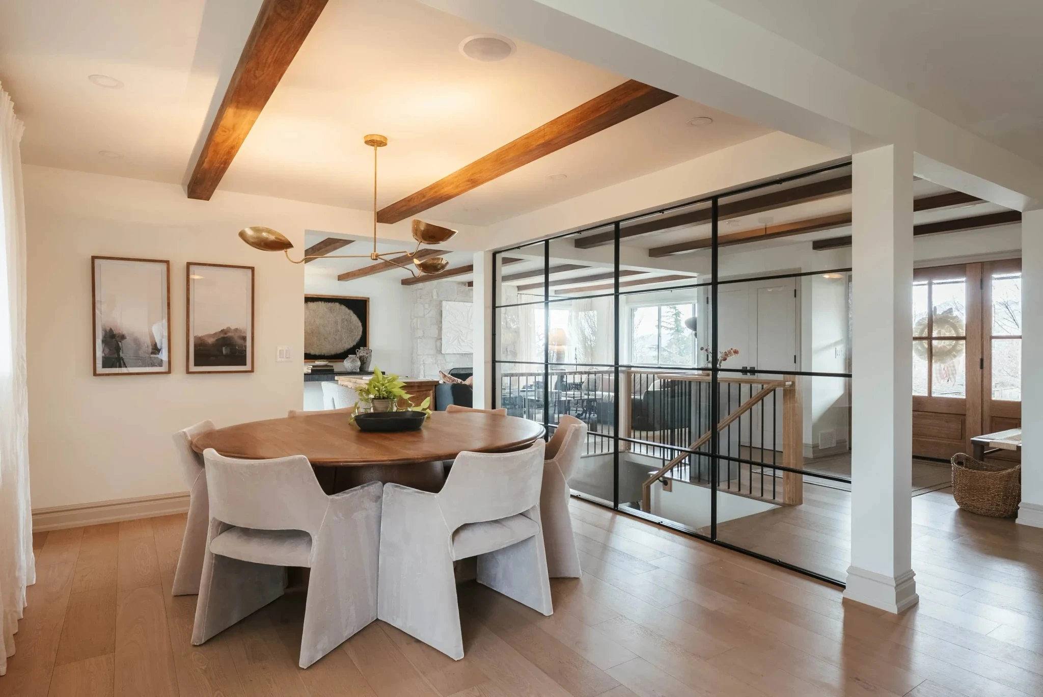 Timber-beamed dining room with black steel and glass partition beside an open stair